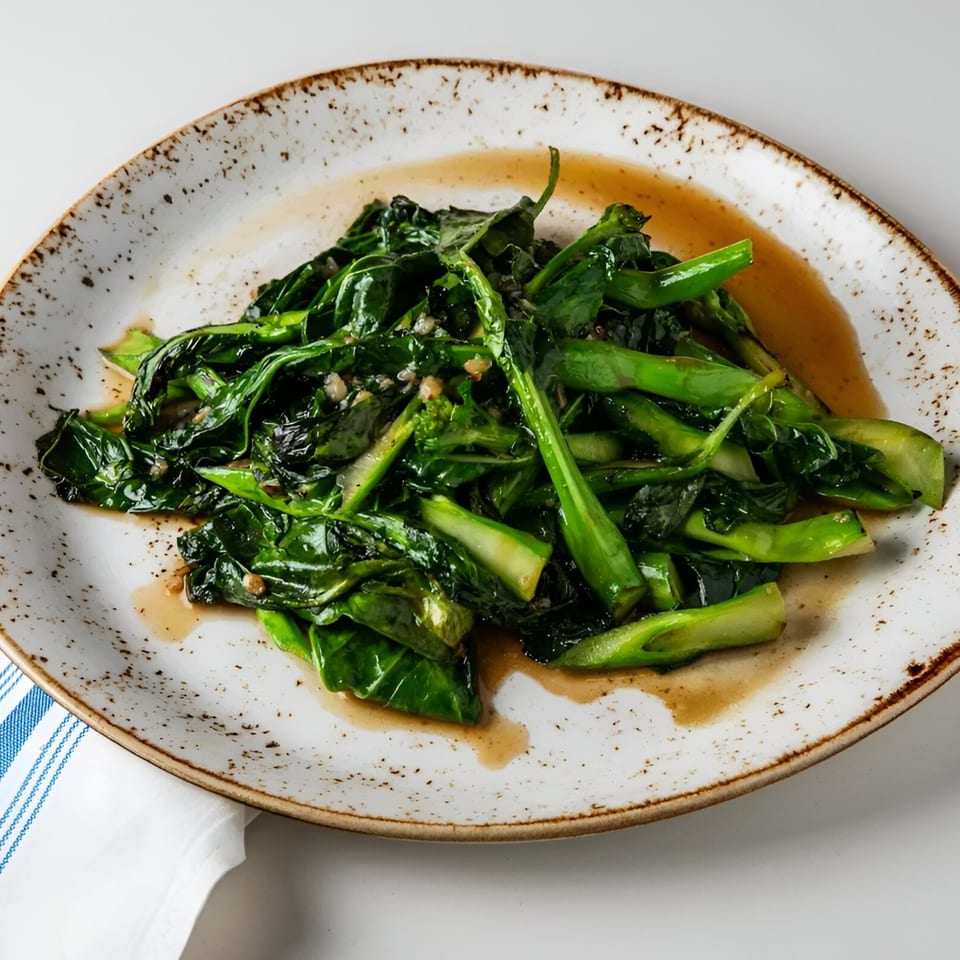 Stir-fried Chinese broccoli with garlic and sauce on a speckled white plate at Osha Thai Kitchen.