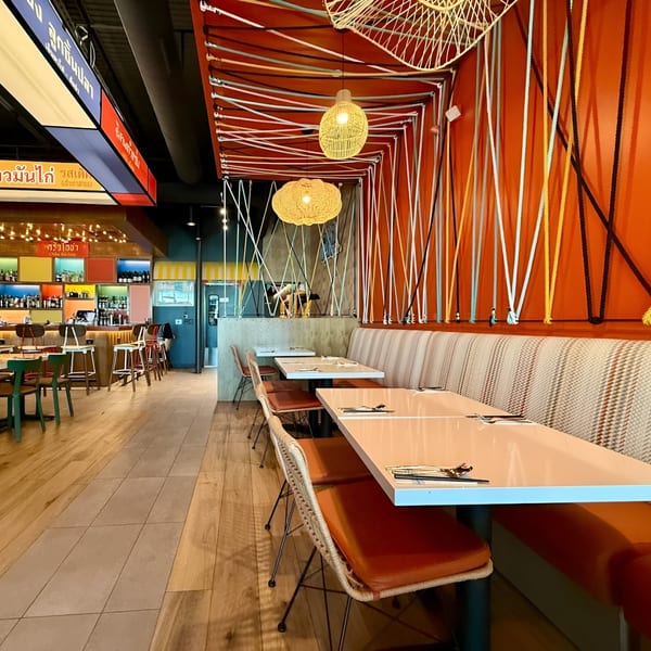 Osha Thai Kitchen interior with orange walls, colorful ropes, wicker lights, and a bar area.