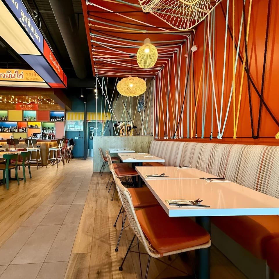 Osha Thai Kitchen interior with orange walls, colorful ropes, wicker lights, and a bar area.