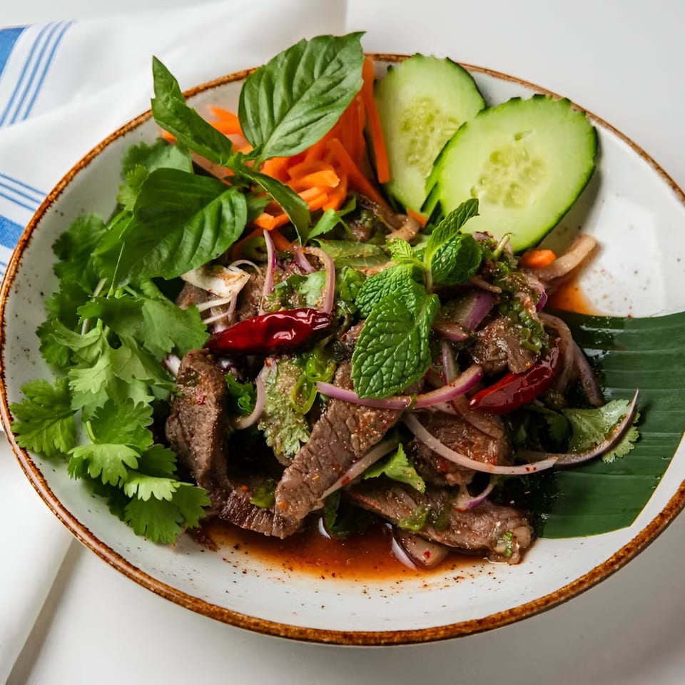 Osha Thai Kitchen's spicy beef salad with red onions, mint, cilantro, and chili on a white plate.